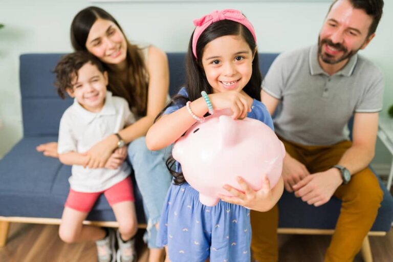 a group of people sitting on a couch and smiling at a girl holding a piggy bank- how to teach your kids about money