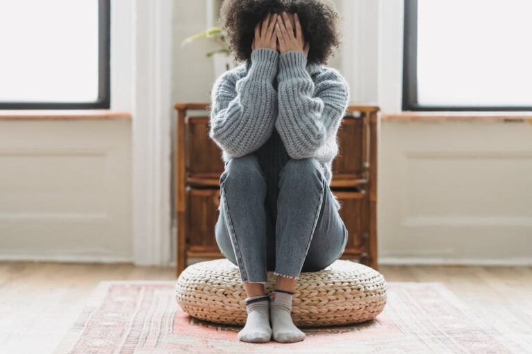 a woman sitting on a pouf with her hands over her face