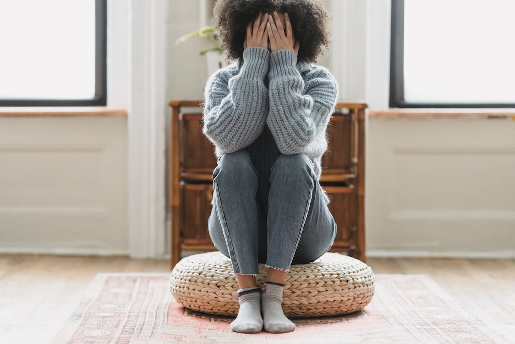 a woman sitting on a pouf with her hands over her face